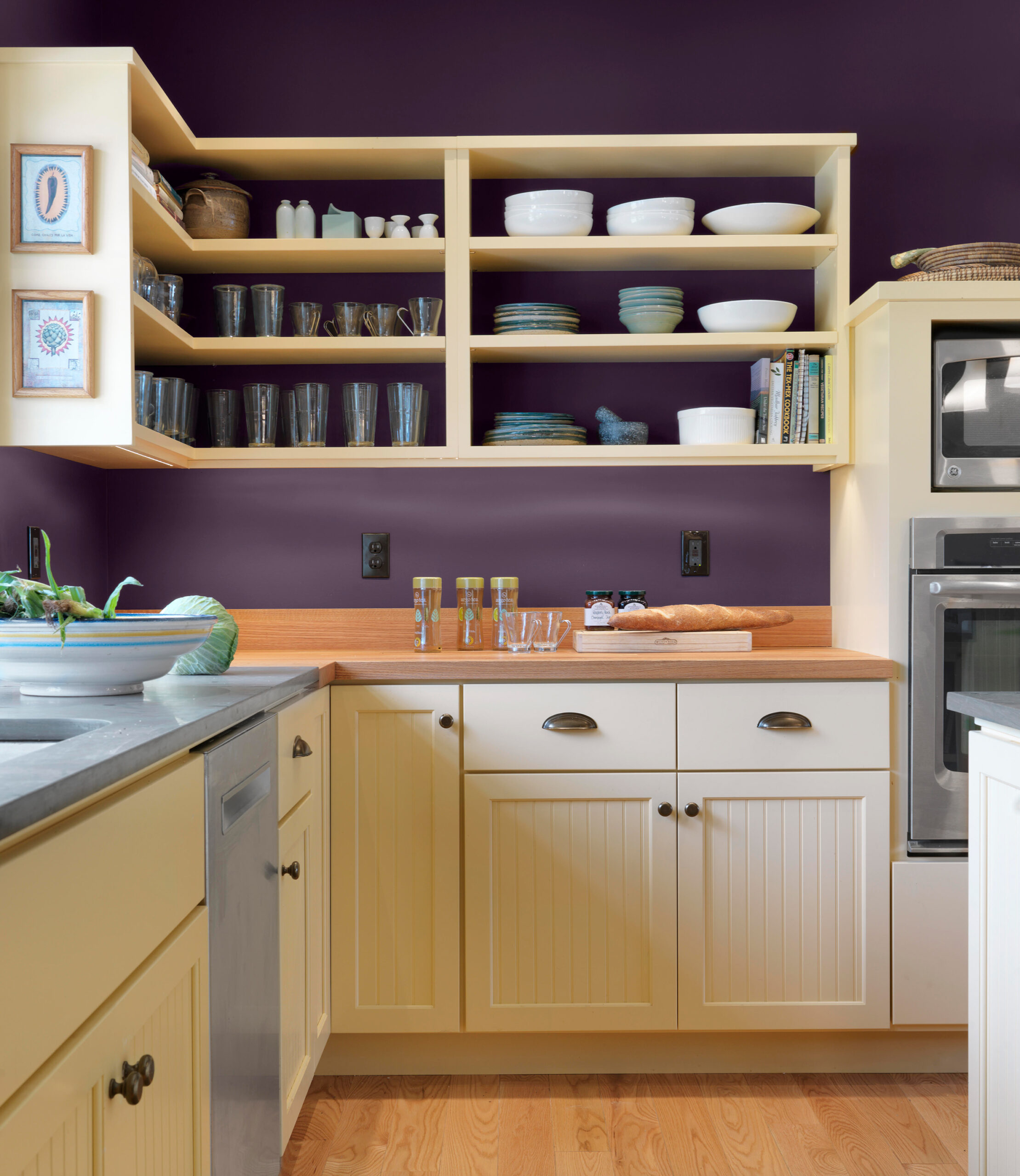 A kitchen with shelves and framed phots with a yellow and violet color scheme.